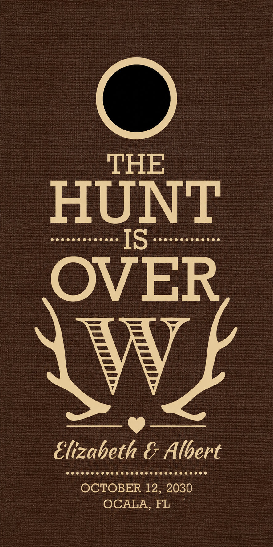 A cornhole board with a circular cutout at the top, featuring the phrase 'THE HUNT IS OVER' in beige lettering, antler graphics, the names 'Elizabeth & Albert,' and the date/location 'OCTOBER 12, 2030 / Ocala, FL.'.
