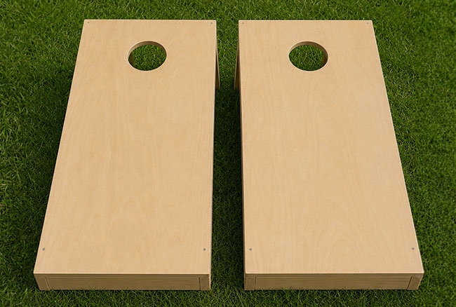 Two unfinished light wood cornhole boards with circular holes, shown side by side on green grass.