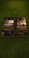 Two cornhole boards with a rustic forest and sunrise landscape print, displayed side-by-side on a green grass background.
